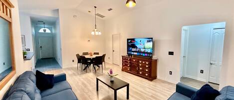A living room with a TV, sofas, a coffee table, and a dining area.