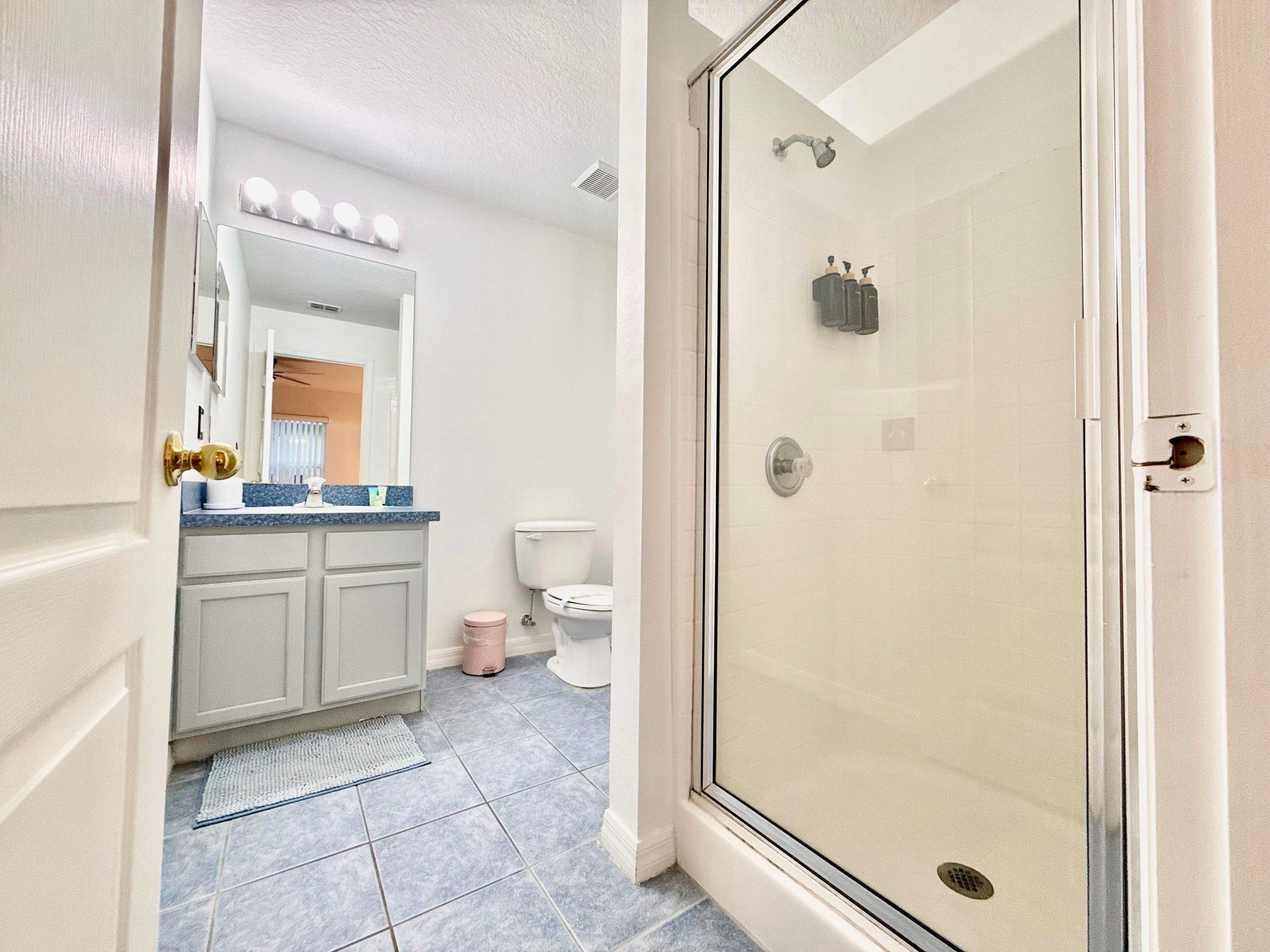 A bathroom with a glass-enclosed shower, a white toilet, and a vanity with a mirror and lights.