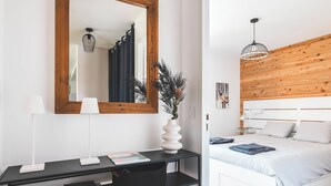 A modern bedroom with a wooden headboard, a white bed, and a desk with a mirror and lamp.