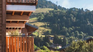 A wooden balcony with a view of a hilly landscape and houses in the background.