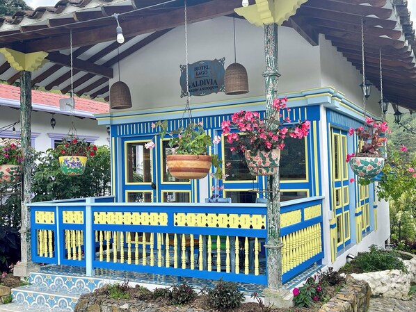 A colorful building with a blue and yellow facade, hanging flower baskets, and a sign indicating it is a hotel. - Hotel Lago Valdivia (Jardin)