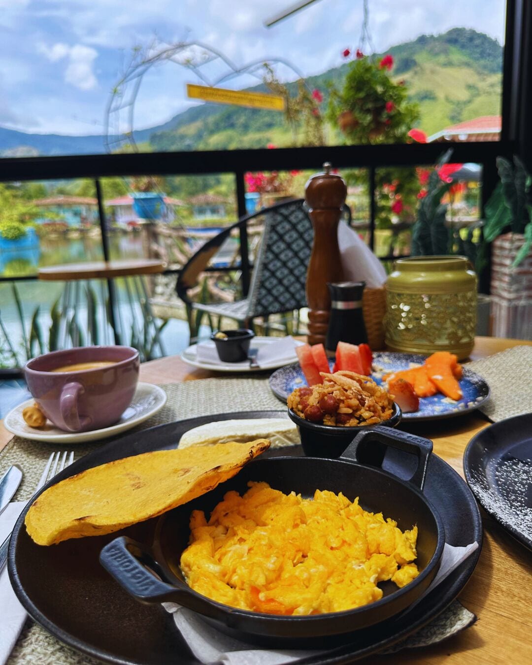 A table with a meal consisting of rice, plantains, and a small bowl of beans, set against a scenic view.