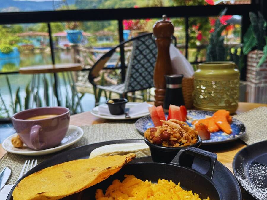 A table with a meal consisting of rice, plantains, and a small bowl of beans, set against a scenic view.