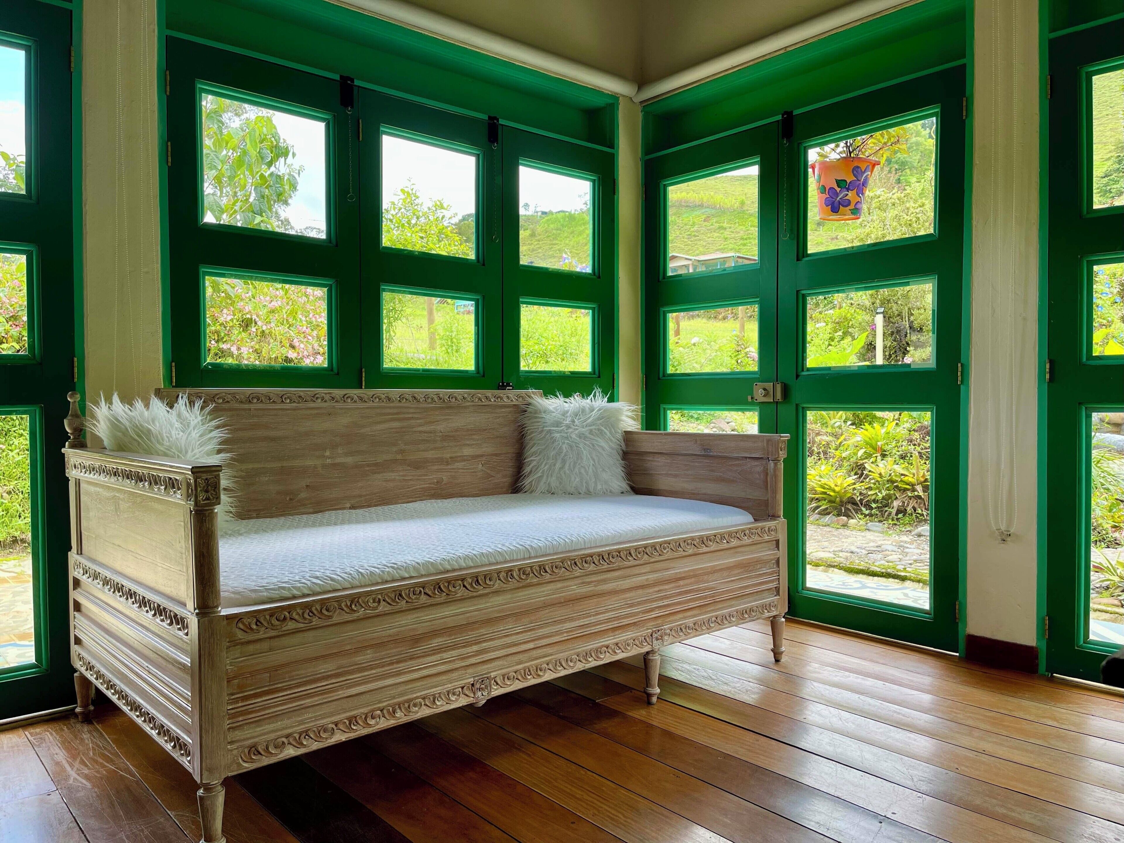 A room with a wooden bench, green doors, and windows with a view of greenery.
