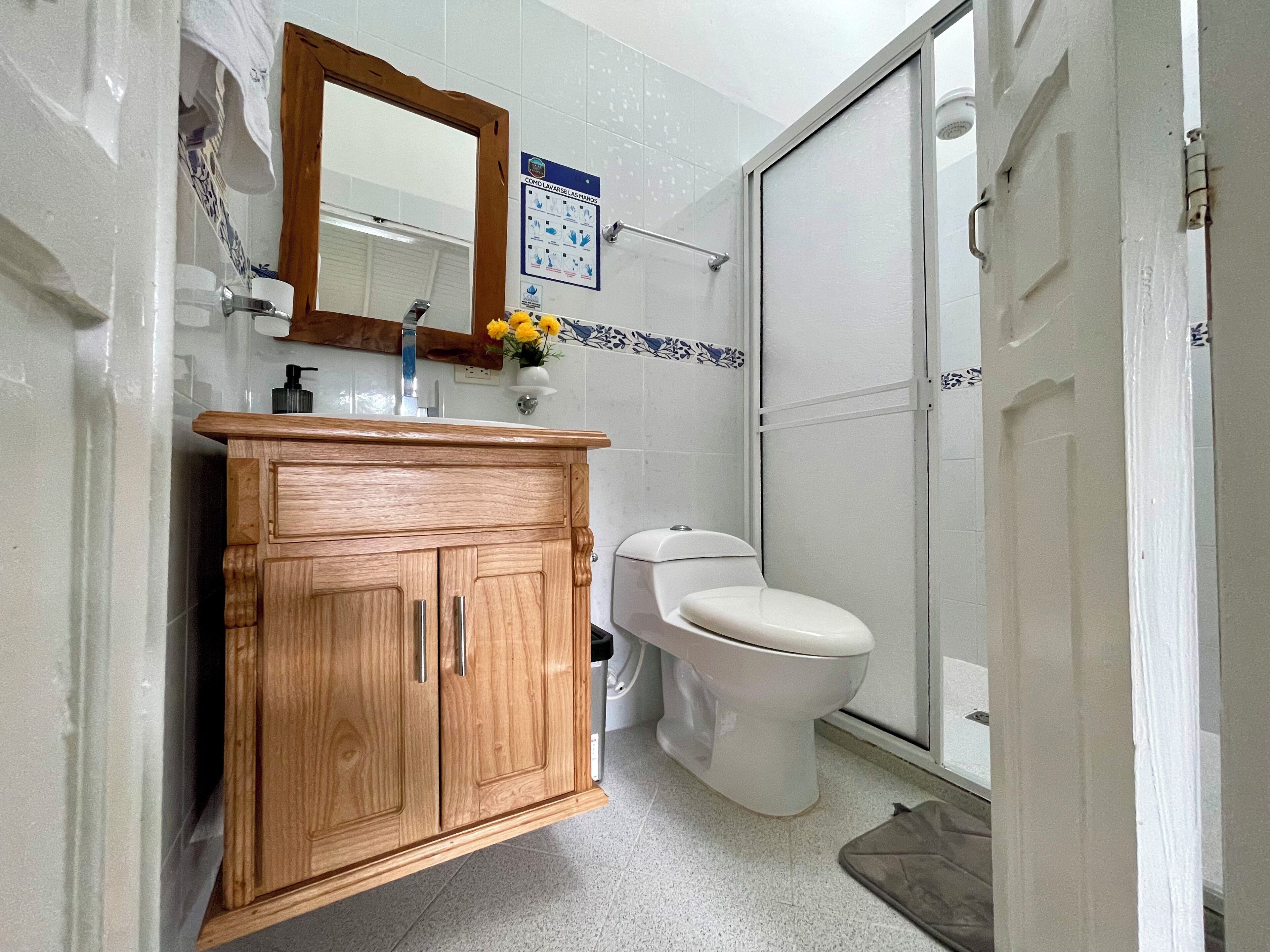 A bathroom with a wooden vanity, a toilet, a shower, and a mirror.