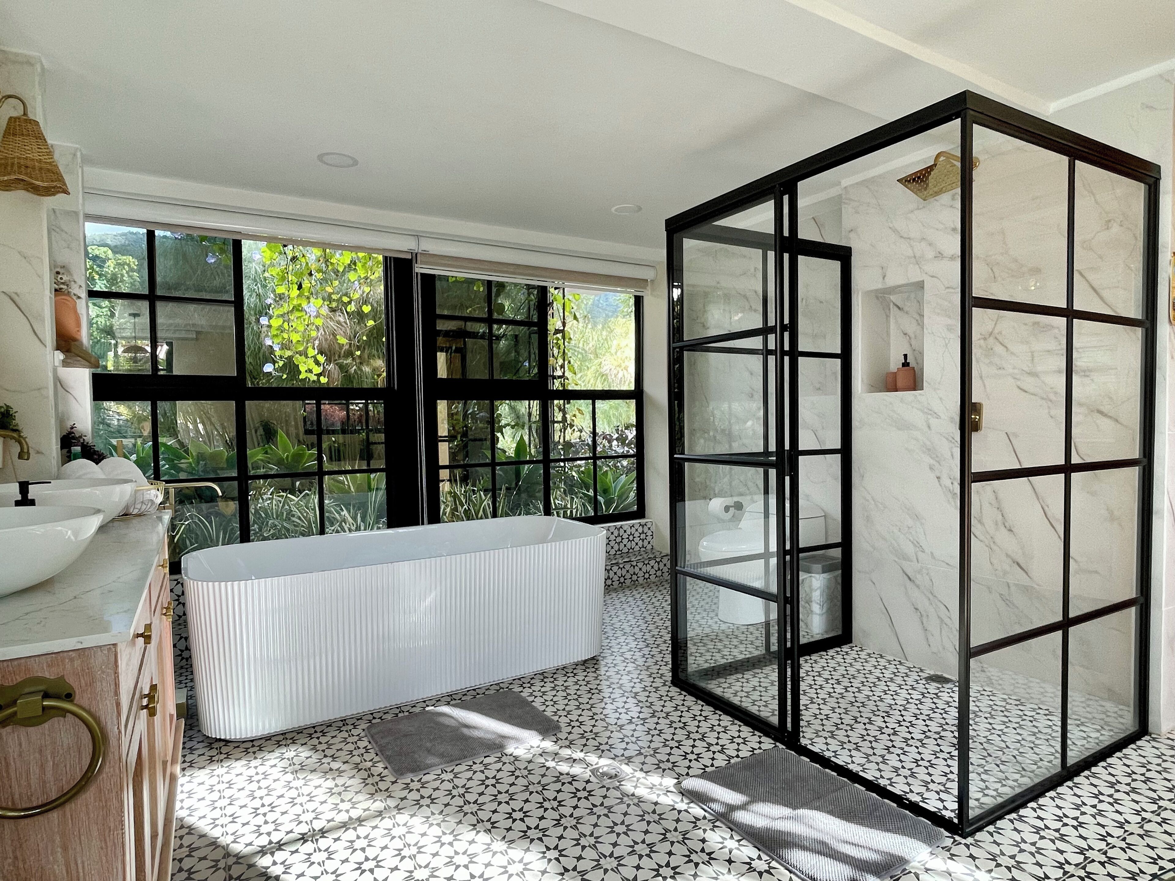 Ein modernes Badezimmer mit einer großen Badewanne, einer Duschkabine aus Glas und Blick auf Grün durch großzügige Fenster.