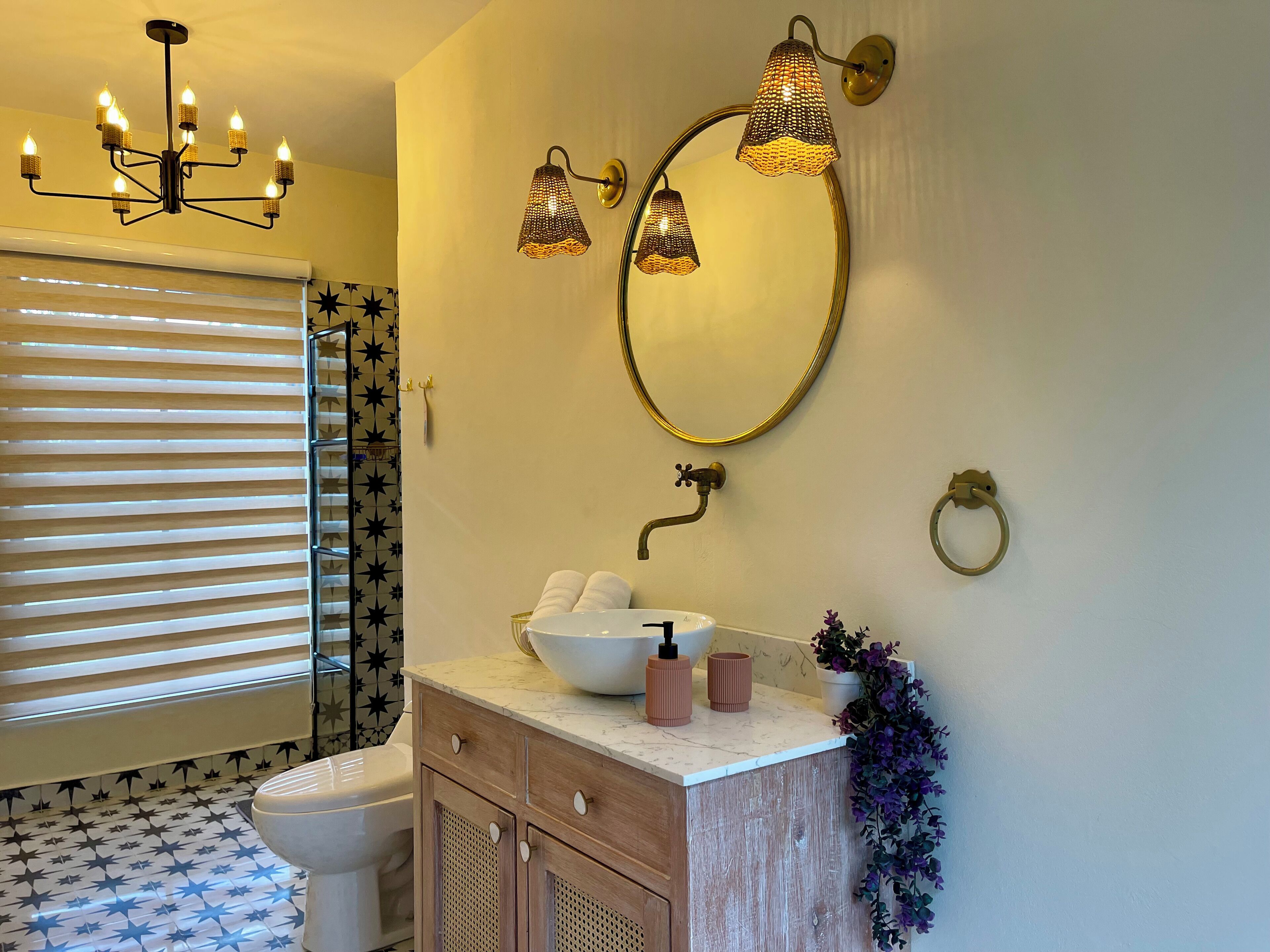 Een badkamer met een vloer met stervenspatroon, een wit toilet, een houten wastafelmeubel met een witte wastafel en een kroonluchter.