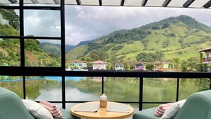 Ein Zimmer mit zwei grünen Sesseln, die zu einem großen Fenster mit Blick auf einen See und bunte Häuser ausgerichtet sind.