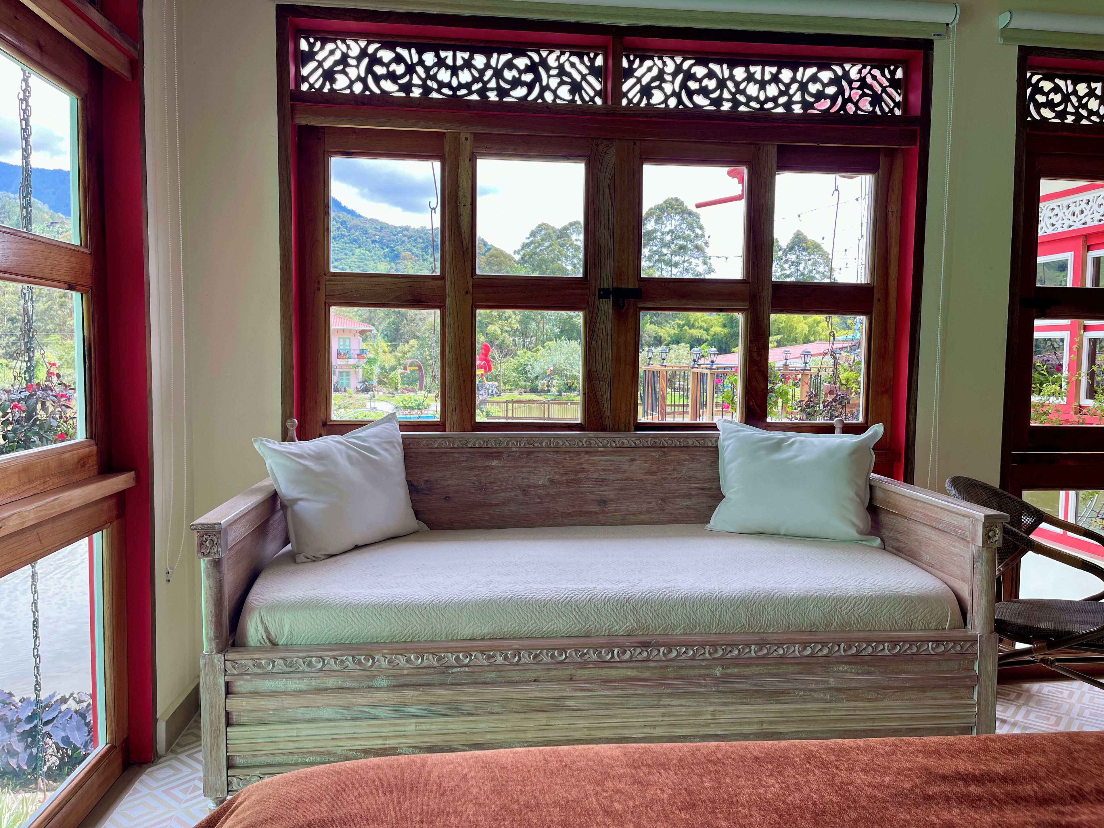 A wooden sofa bed with white cushions, positioned in front of a window with a decorative wooden frame.