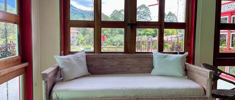 A wooden sofa bed with white cushions, positioned in front of a window with a decorative wooden frame.