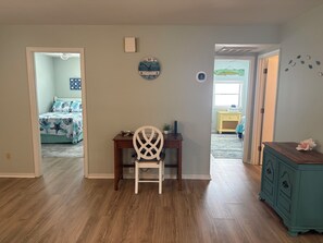 Quarto com piso de madeira, escrivaninha com cadeira, cama com colcha temática de estrela-do-mar, relógio de parede e pequeno armário.