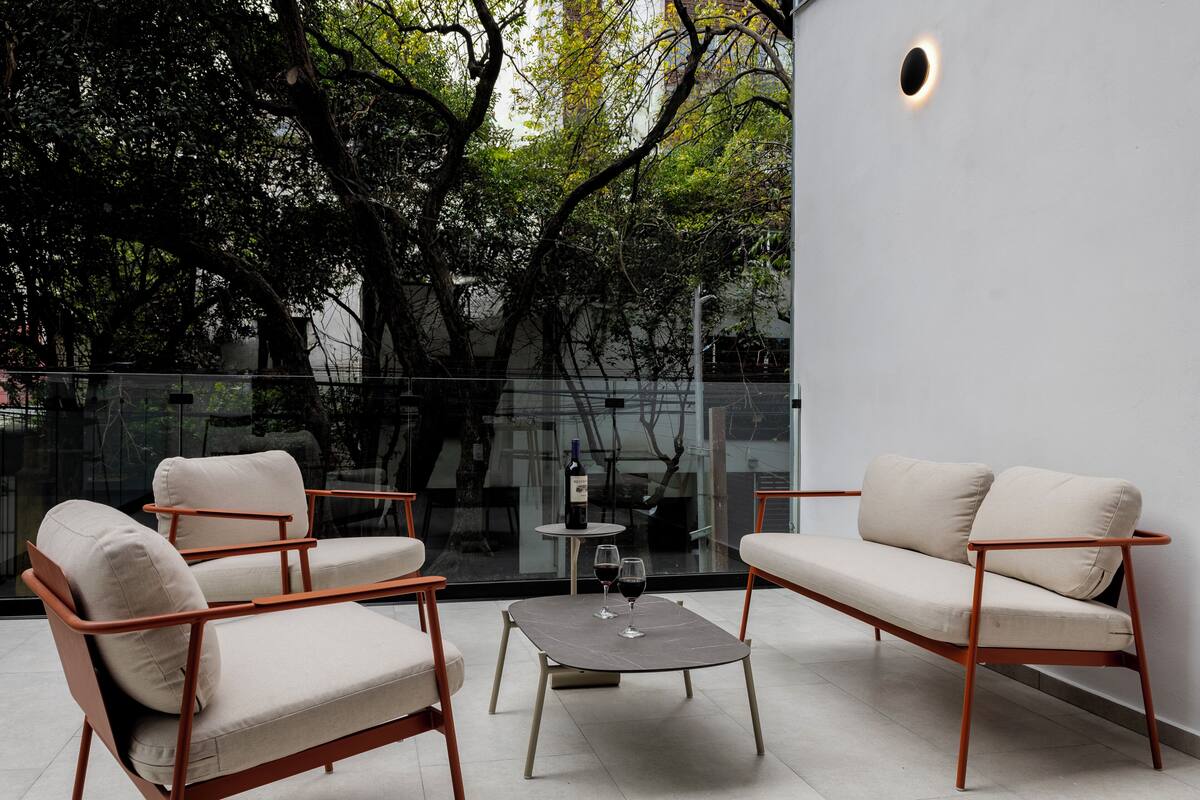 Un área de estar moderna al aire libre, con un separador de vidrio, dos sofás y una pequeña mesa con copas de vino.
