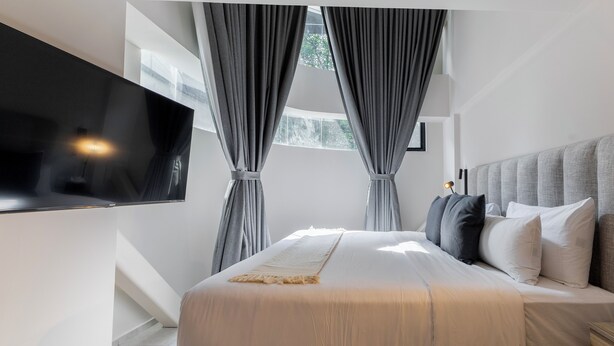Un dormitorio moderno con una cama grande, cortinas grises, un televisor montado y vistas a zonas verdes.
