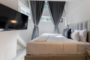 A modern bedroom with a large bed, grey curtains, a mounted TV, and a view of greenery outside. - Capitalia Hipodromo Condesa (Mexico City)