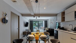 Una cocina moderna con comedor, que cuenta con una mesa de vidrio, sillas oscuras y una jarra naranja en el centro.