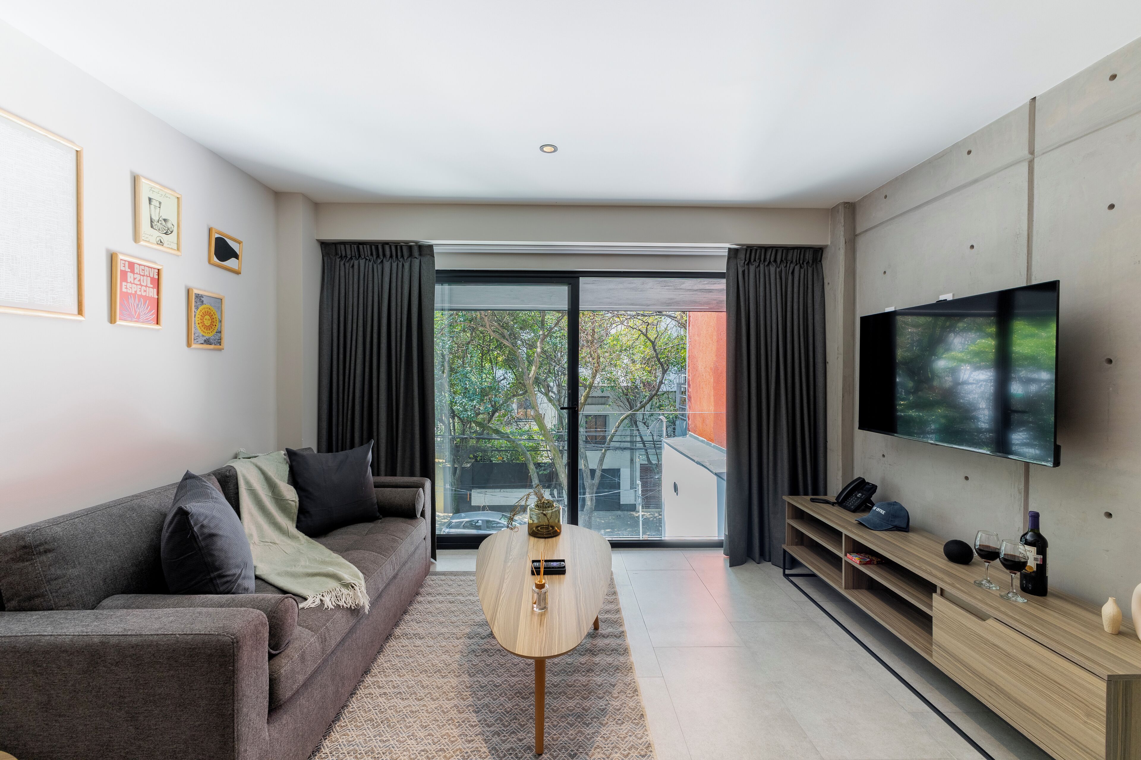 A modern living room with a sofa, a coffee table, a flat-screen TV, and a sliding glass door leading to an outdoor area.
