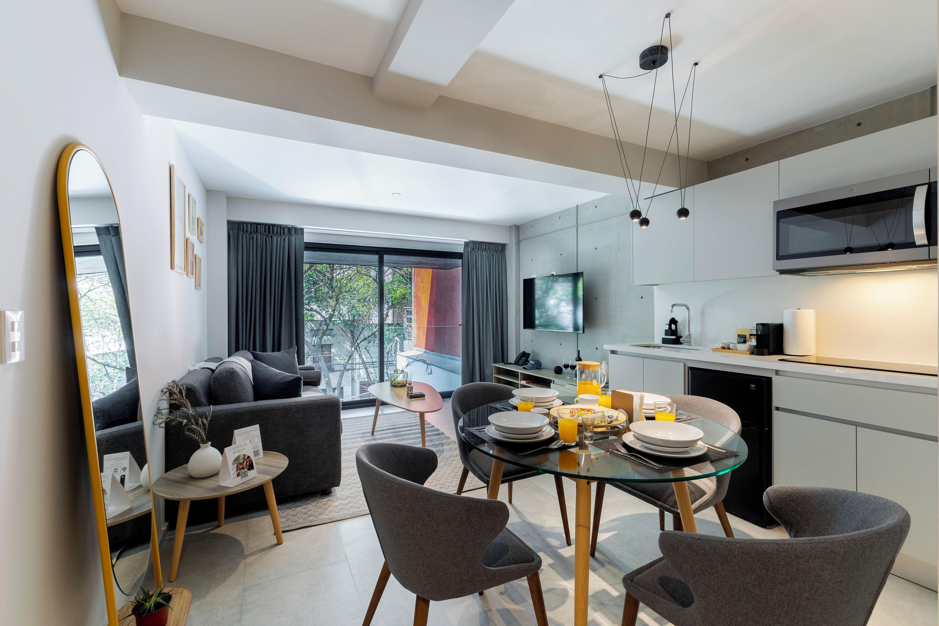 A modern kitchen with a dining area, large windows, and a flat-screen TV.