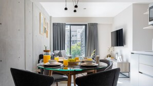Un comedor moderno con una mesa de vidrio, sillas grises y vistas de la ciudad a través de grandes ventanales.
