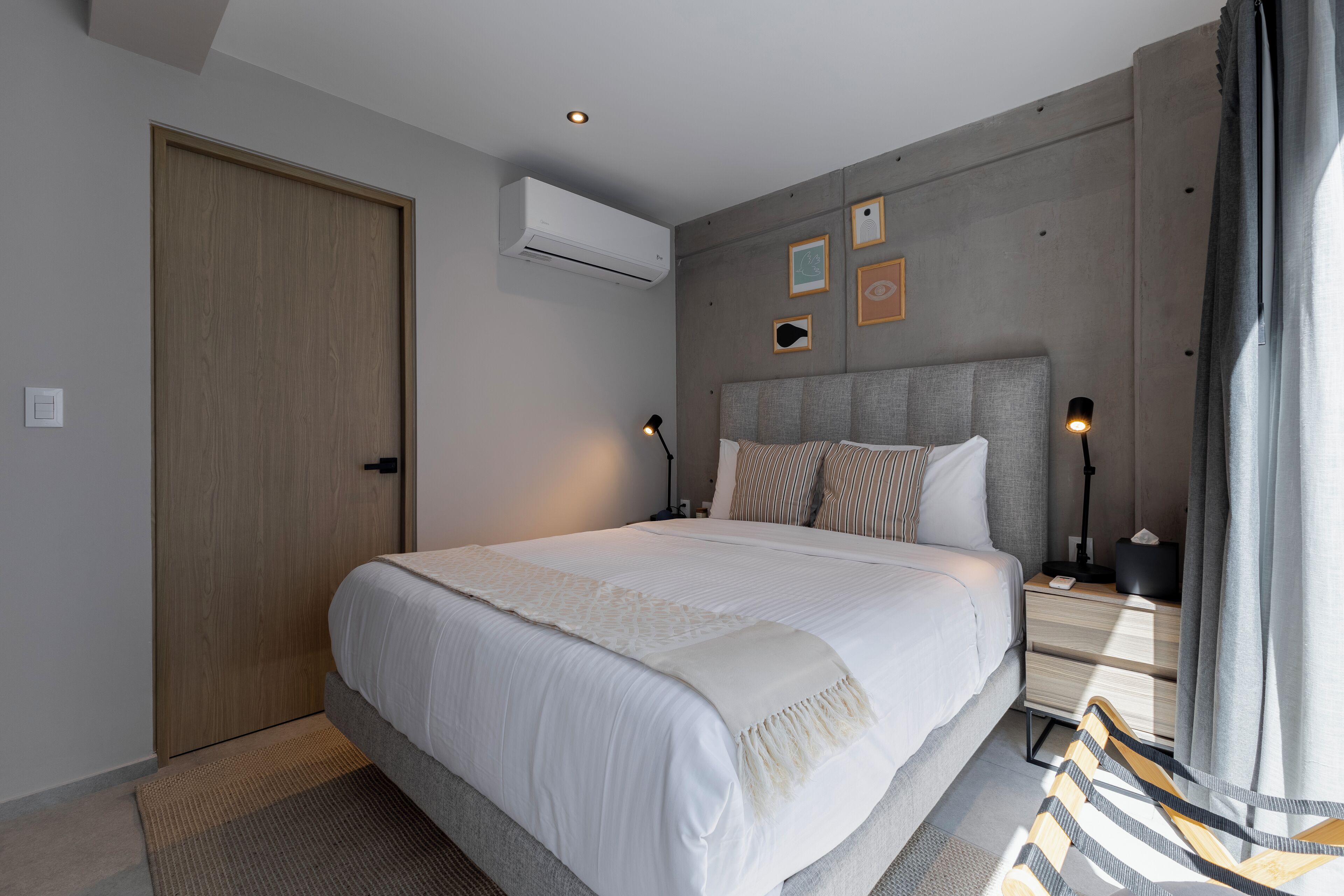 Un dormitorio moderno con una cama grande, mesitas de noche, aire acondicionado y vistas al exterior.