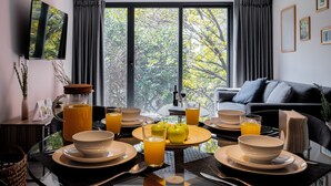 Un comedor moderno con una mesa de vidrio dispuesta para el desayuno, con platos, tazones y vasos de jugo de naranja.