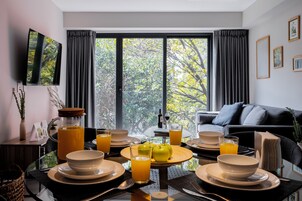 Un coin repas moderne avec une table en verre dressée pour le petit-déjeuner, agrémentée d’assiettes, de bols et de verres de jus d’orange.