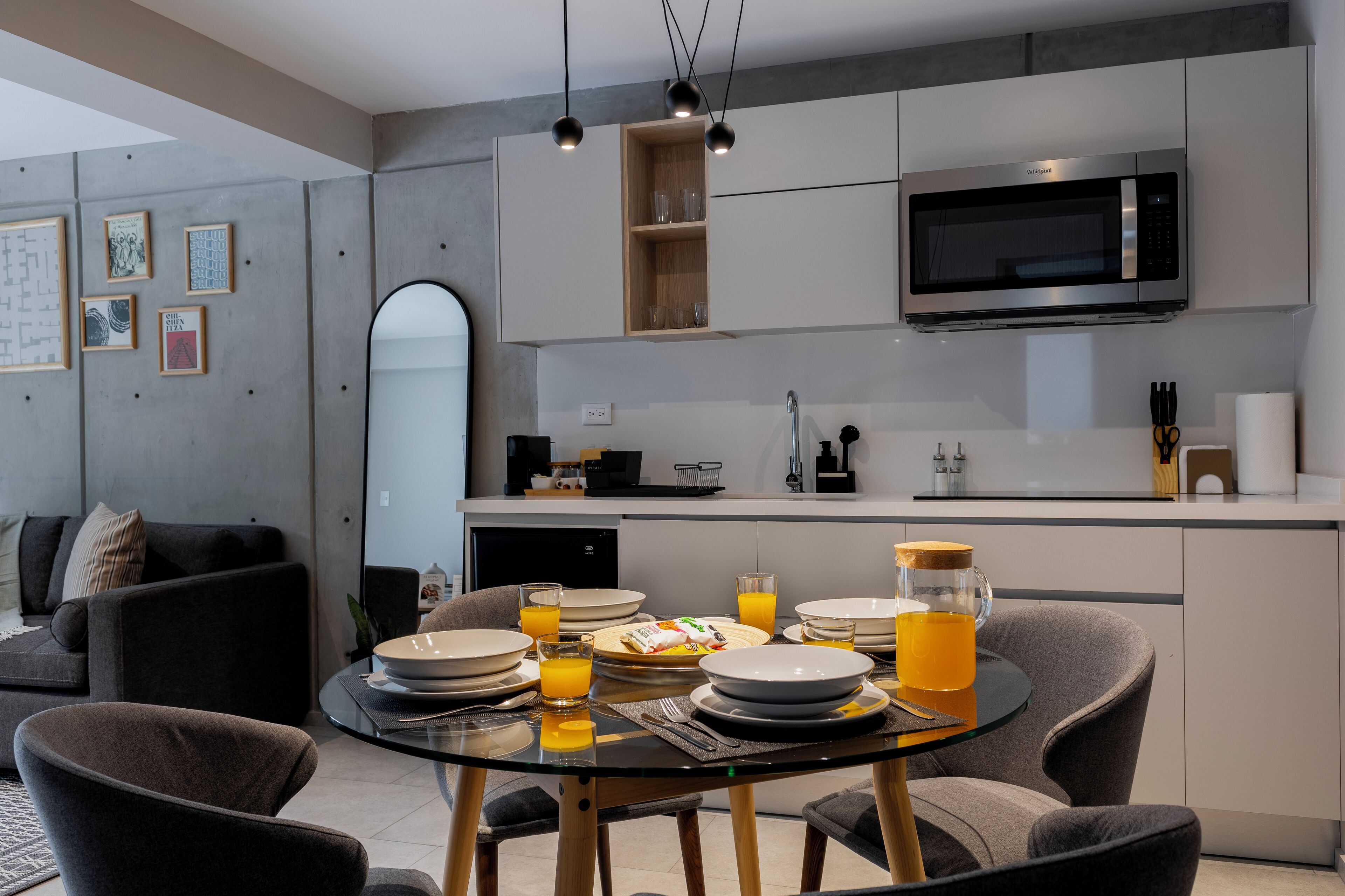 A modern kitchen with a dining area, featuring a glass table, chairs, and a microwave above the counter.