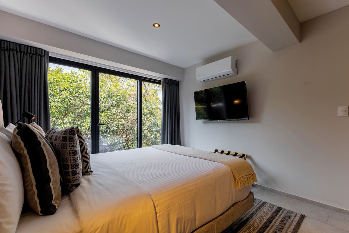 Un dormitorio moderno con una cama grande, un televisor de pantalla plana en la pared y una ventana con cortinas.