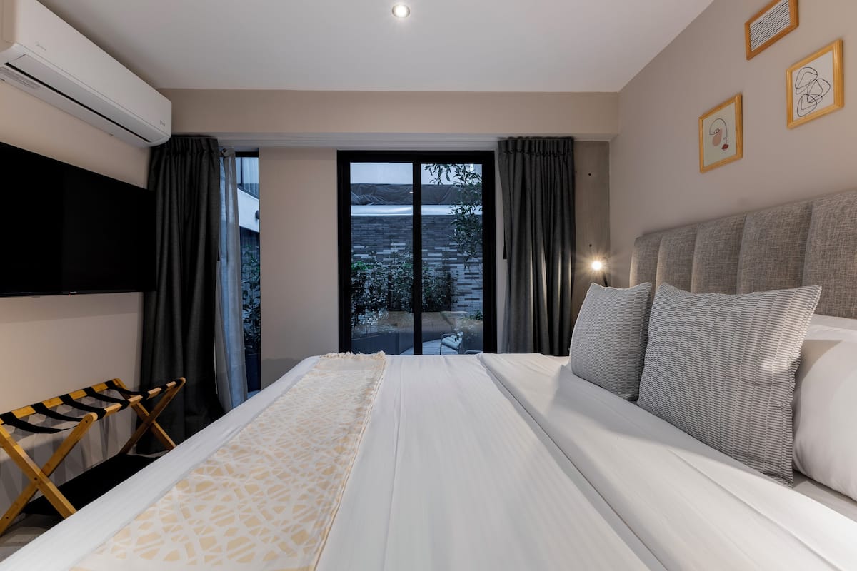 Habitación de hotel con cama, televisión, balcón con cortinas y vistas al exterior.