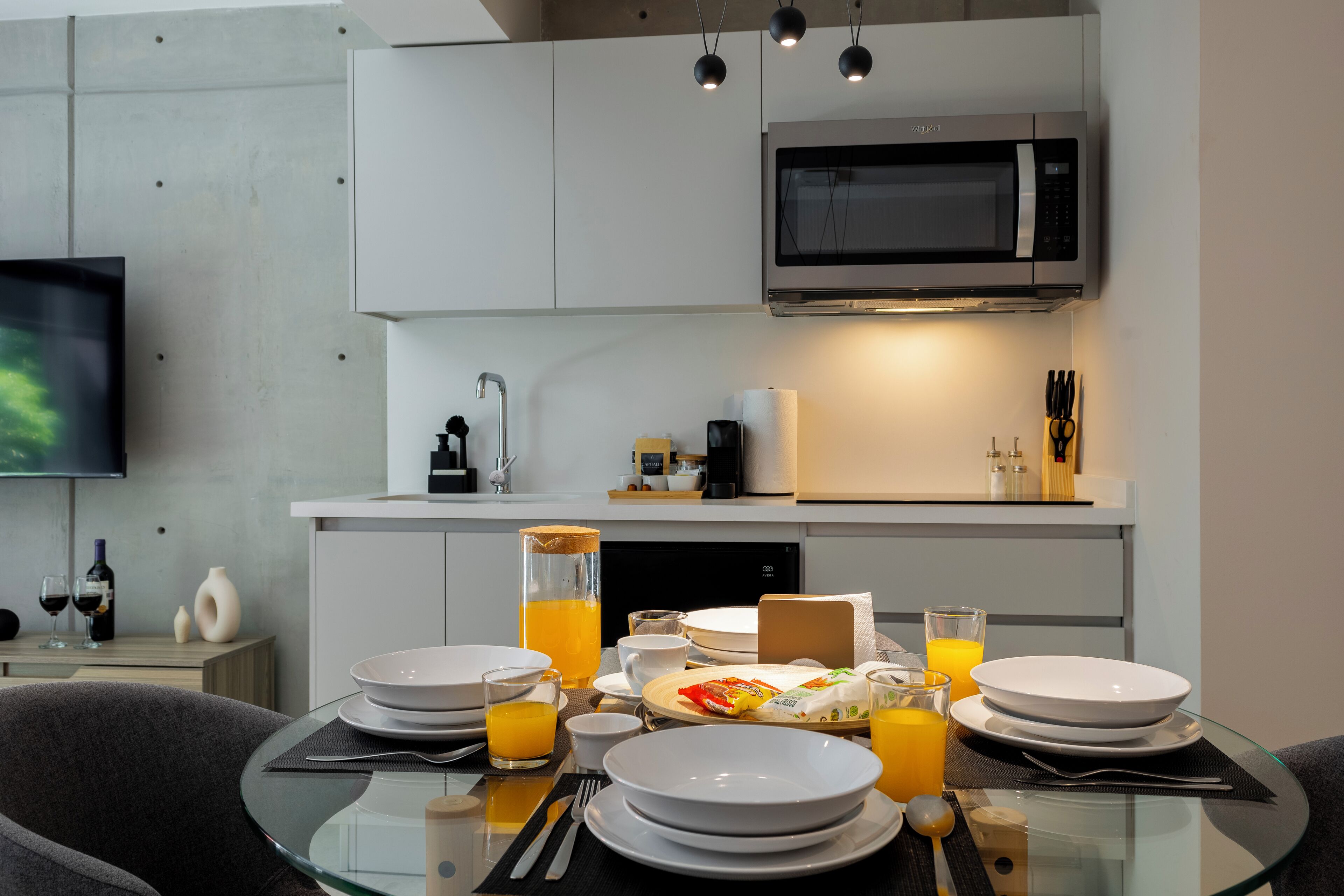 A modern kitchen with a microwave, sink, and dining area with plates, glasses, and a bottle of orange juice.