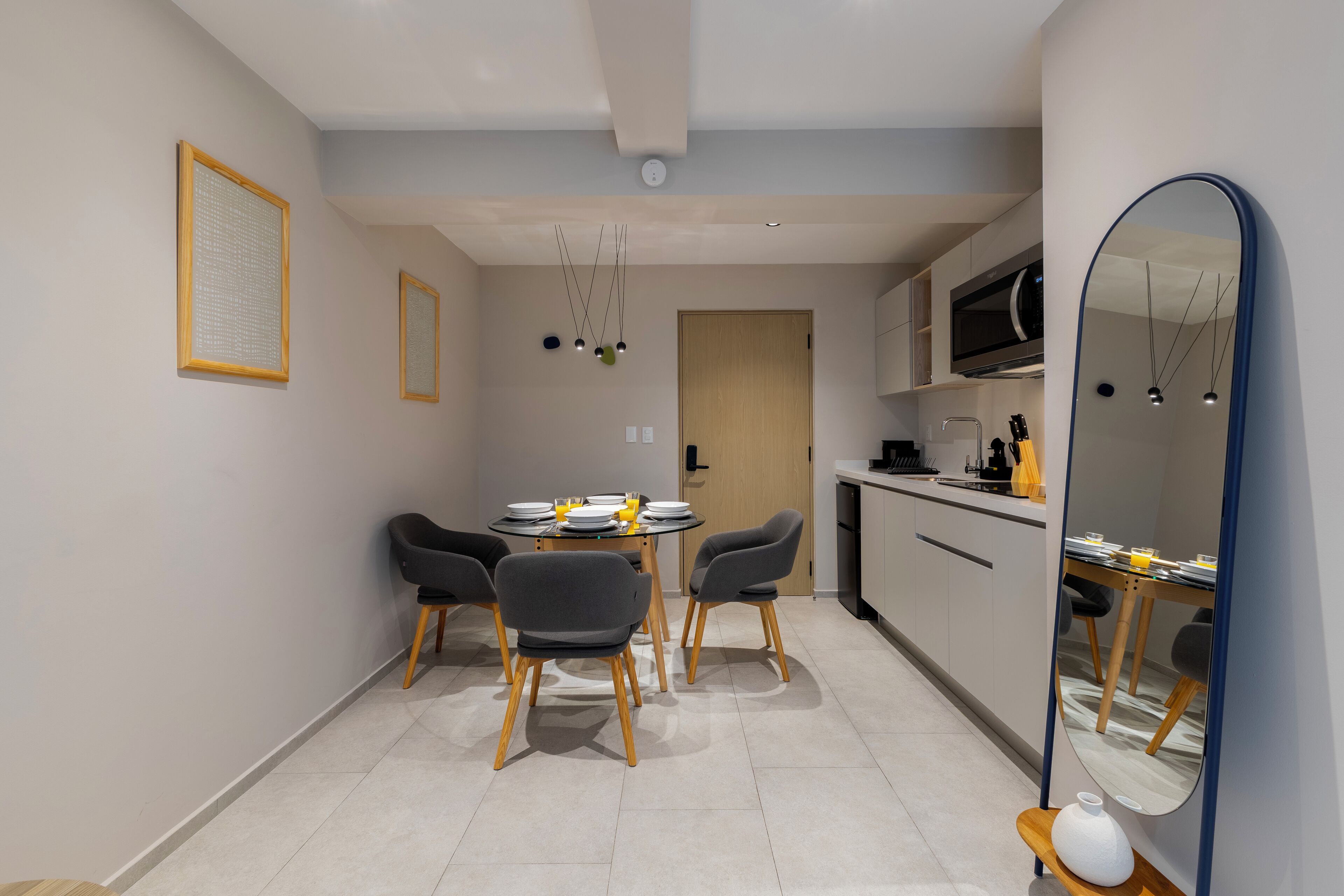 A modern kitchen with a dining area, featuring a round table with chairs, a microwave, and a large mirror.