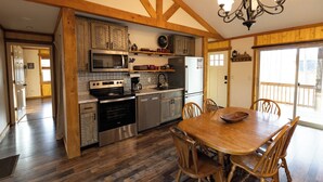 Een keuken met houten balken, een eettafel met stoelen, een kroonluchter en uitzicht door een schuifdeur van glas.