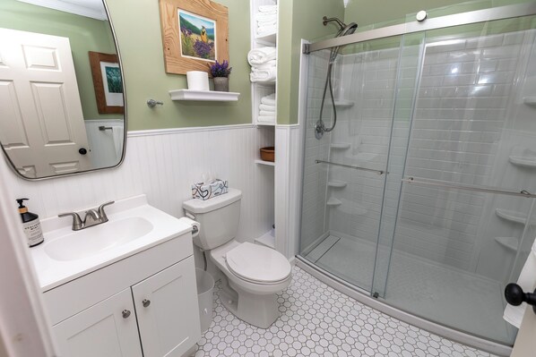 A bathroom with a white sink, toilet, and glass-enclosed shower. There are shelves with towels and toiletries. - Family Mountain Getaway, Stay in the New River Gorge Area, Near Glade Creek Farm (Raleigh County)