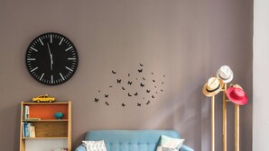 A modern living room with a blue sofa, a round wooden coffee table, a wicker chair, a bookshelf, a large wall clock, and a wall decal of butterflies. - Casa Roma nel cuore di Palermo by Wonderful Italy (Palermo)