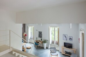 A spacious living area with a staircase, a dining table, chairs, a sofa, a TV, and artwork on the walls. - Casa Roma nel cuore di Palermo by Wonderful Italy (Palermo)