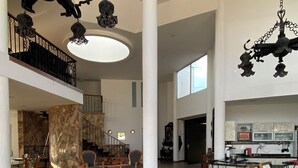 A spacious living area with a high ceiling, a staircase, and a kitchen in the background. - Finca Hotel Castillo del Toro (Armenia)