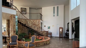 A spacious interior with a central staircase, a dining area with bar stools, and a large window providing natural light. - Finca Hotel Castillo del Toro (Armenia)