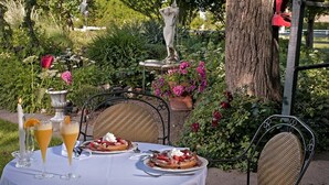 Un espace de restauration en plein air avec une table dressée pour deux personnes, comprenant un dessert et deux boissons.