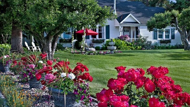 Une maison avec une pelouse bien entretenue, un parasol rouge et une fontaine en pierre.