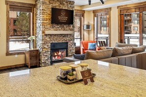 A cozy living room with a stone fireplace, a comfortable sofa, and a coffee table with a tray of amenities. - Moonlight Pooldeck - Trailhead’s Premier Resort Condo w Gondola Access (Steamboat Springs)