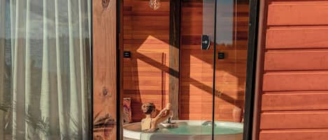 Een houten blokhut met een glazen deur naar een zonaanlegplaats met een jacuzzi.
