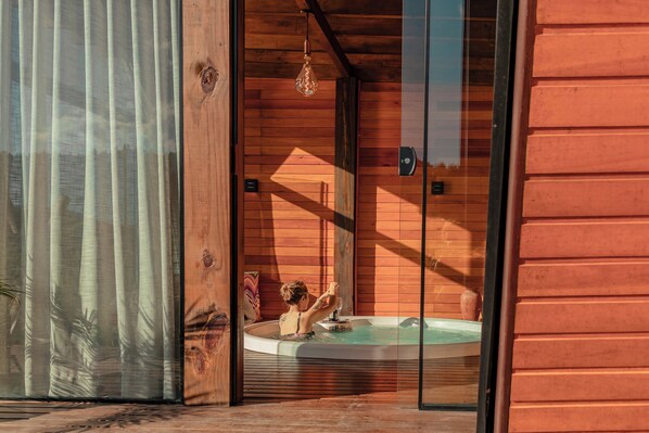 Une cabane en bois avec une porte en verre donnant accès à un espace équipé d’un bain à remous.
