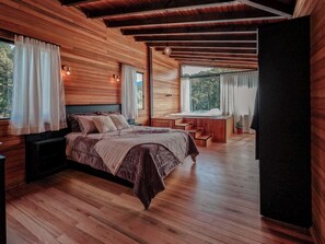 Une chambre à coucher aux murs lambrissés, avec un lit, un petit bureau et une fenêtre avec des rideaux.