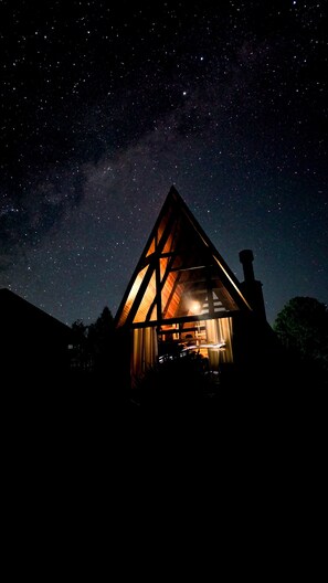Un bâtiment de forme triangulaire, dont l’intérieur est visible et éclairé d’une lumière chaleureuse, se détachant sur un ciel nocturne étoilé.