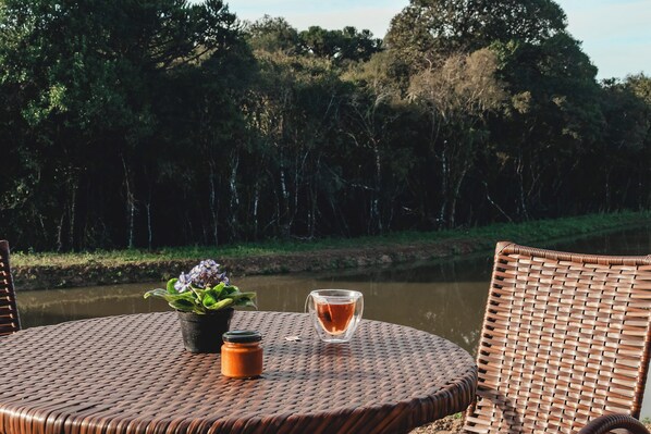A wicker table with a glass of tea, a small potted plant, and a jar. - Cabanas Doce Recanto (Bom Retiro)