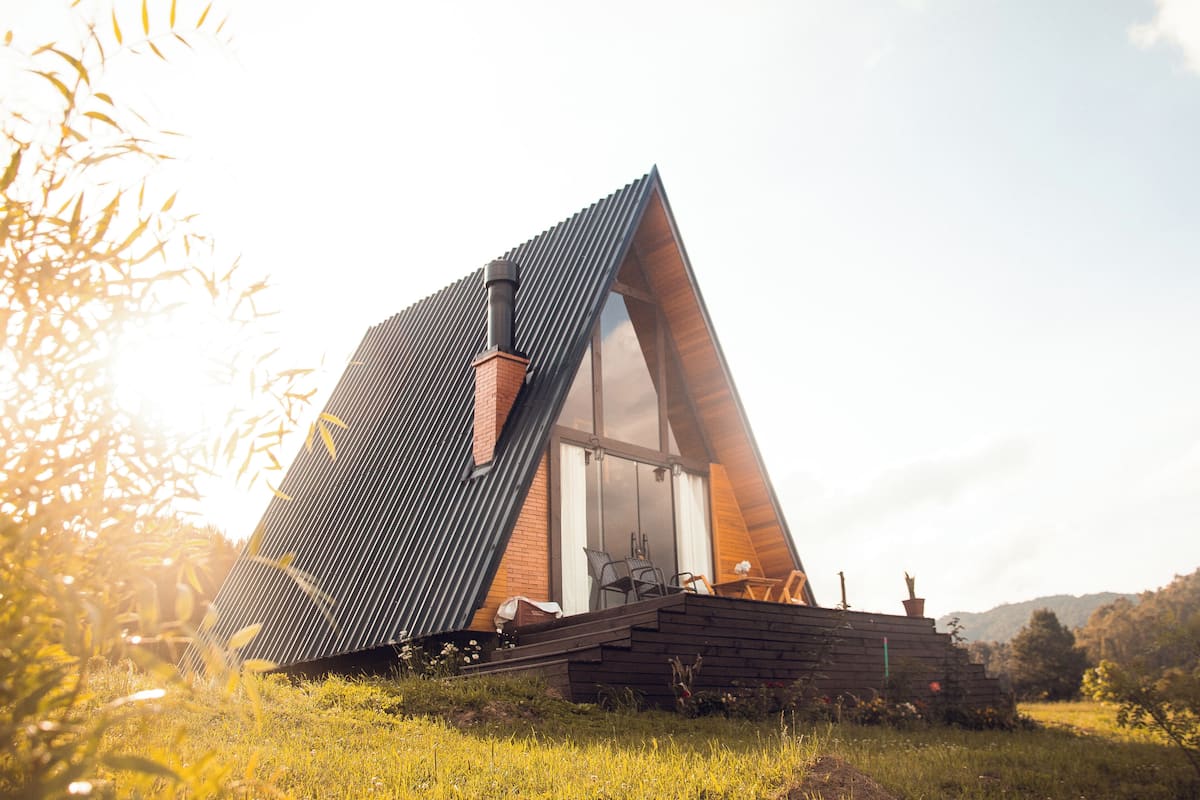 A modern, triangular-shaped house with a large glass window, a chimney, and a wooden deck.