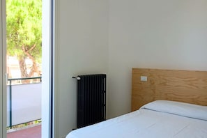 A hotel room with a bed, a radiator, and a window with a view of trees.