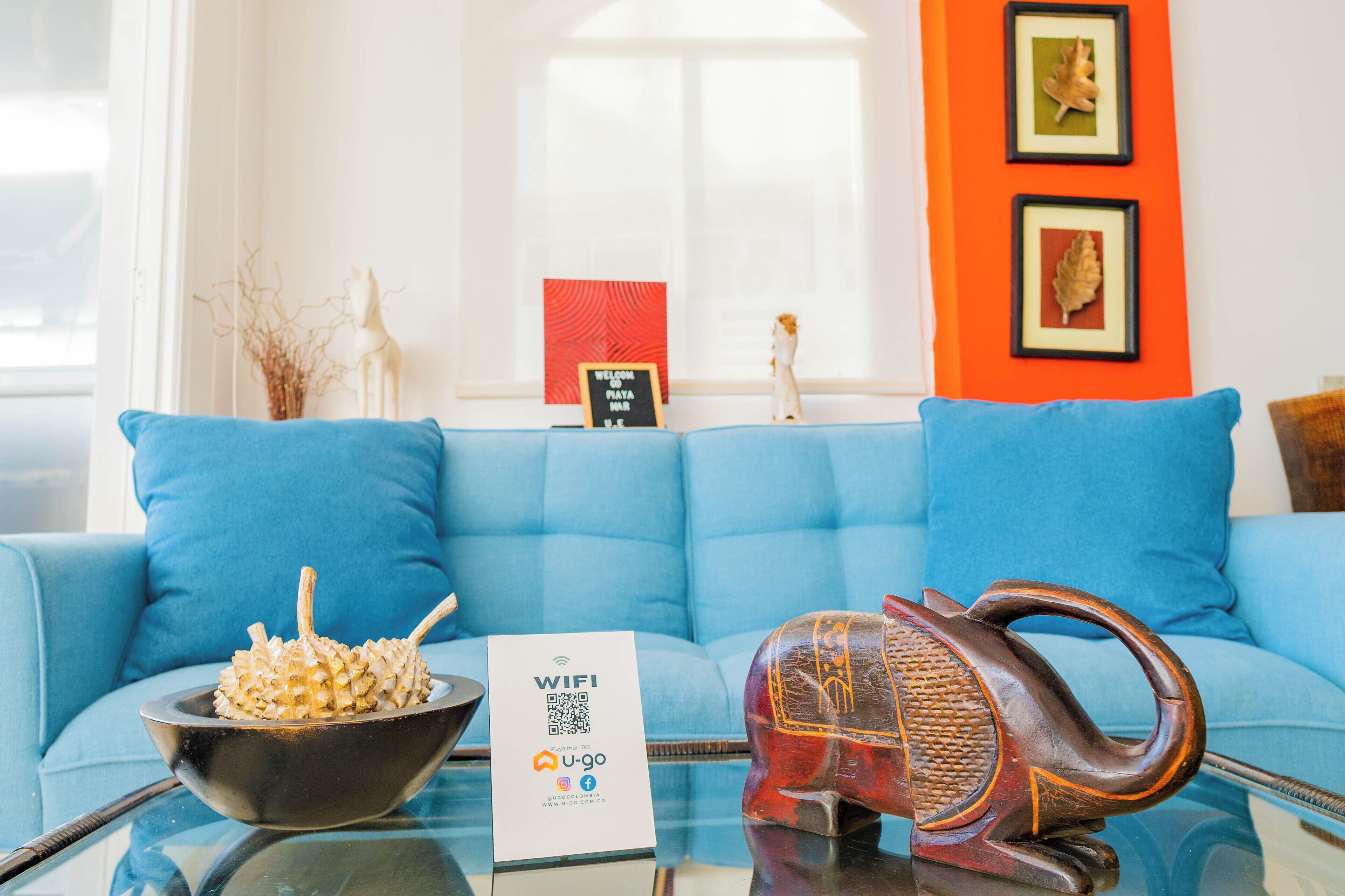 A room with a blue sofa, a decorative bowl, a sign with a QR code, and a framed picture on the wall.