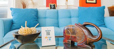 A room with a blue sofa, a decorative bowl, a sign with a QR code, and a framed picture on the wall.