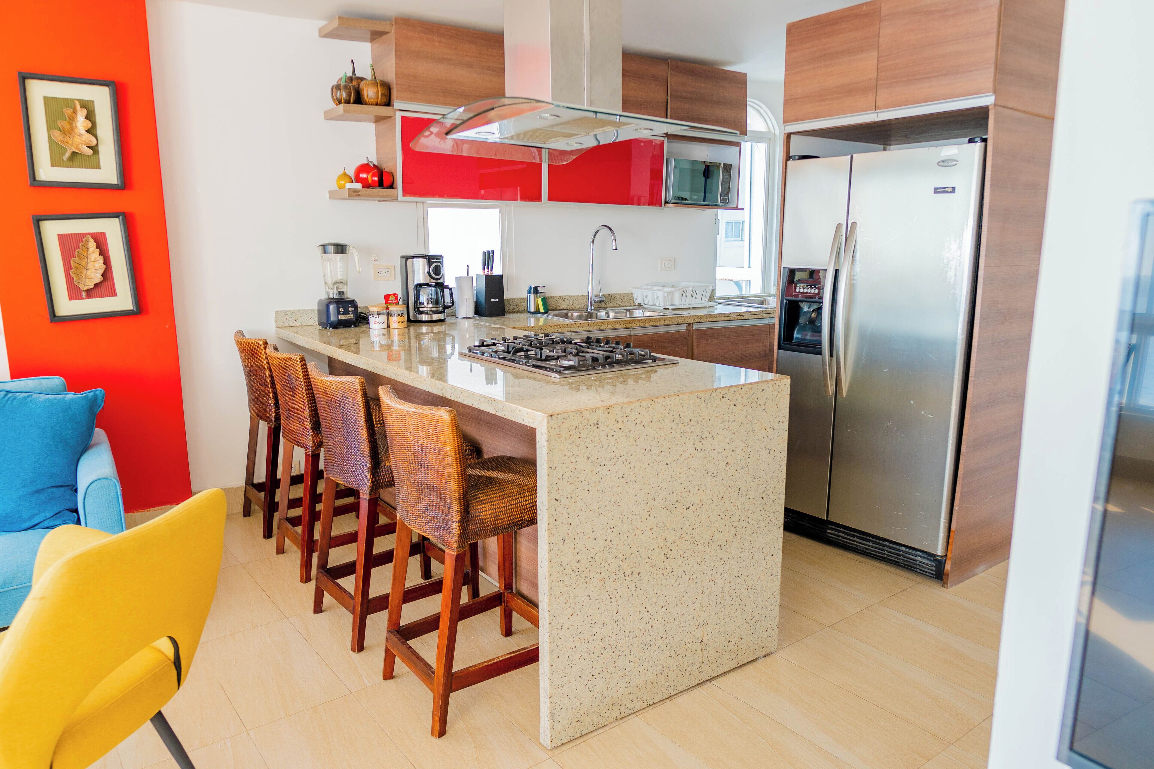 A modern kitchen with a central island, bar stools, a refrigerator, and a coffee maker.