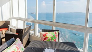 Ein Balkon mit Korbmöbeln und einem Tisch, der Blick auf die Küste mit Booten und einem klaren Himmel bietet.